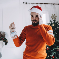 Man in santa's hat stands with a bottle of alcohol