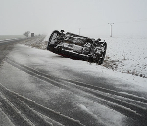 Flipped car on the side of snowy road.