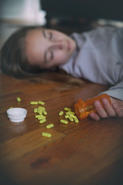 Overdosed teenager girl on a floor with pills.