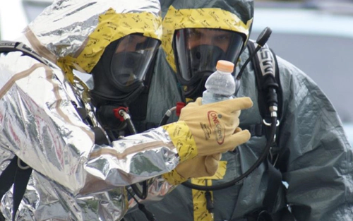 Two people in full haz-mat gear looking at bottle with drugs