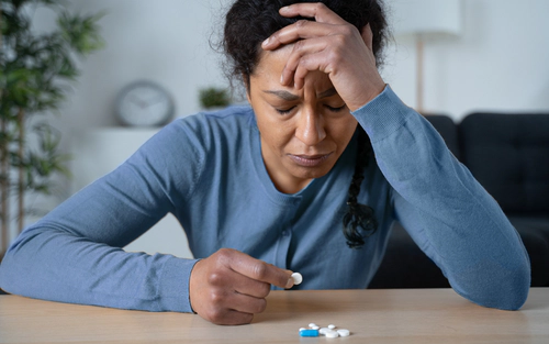Woman at a table, looking at pills while distraught