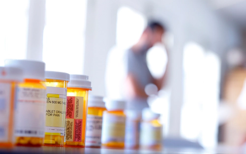 Prescription bottles lined up with man in background